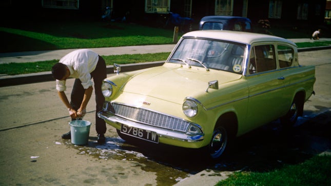 Ein junger Mann wäscht Anfang der 1960er Jahre den Familienwagen Ford Anglia auf einem Anwesen in Essex